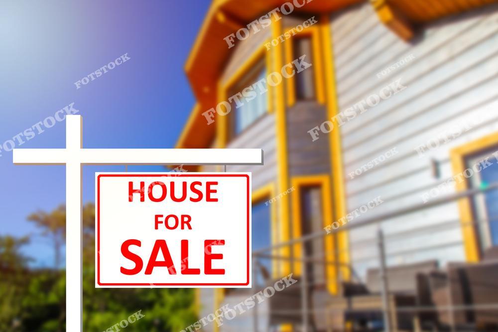 На переднем плане изображен знак "House for Sale" красного цвета на белой стойке. На заднем плане виден загородный деревянный дом с современным дизайном в окружении природы. Композиция символизирует возможности покупки комфортного жилья в живописном месте.